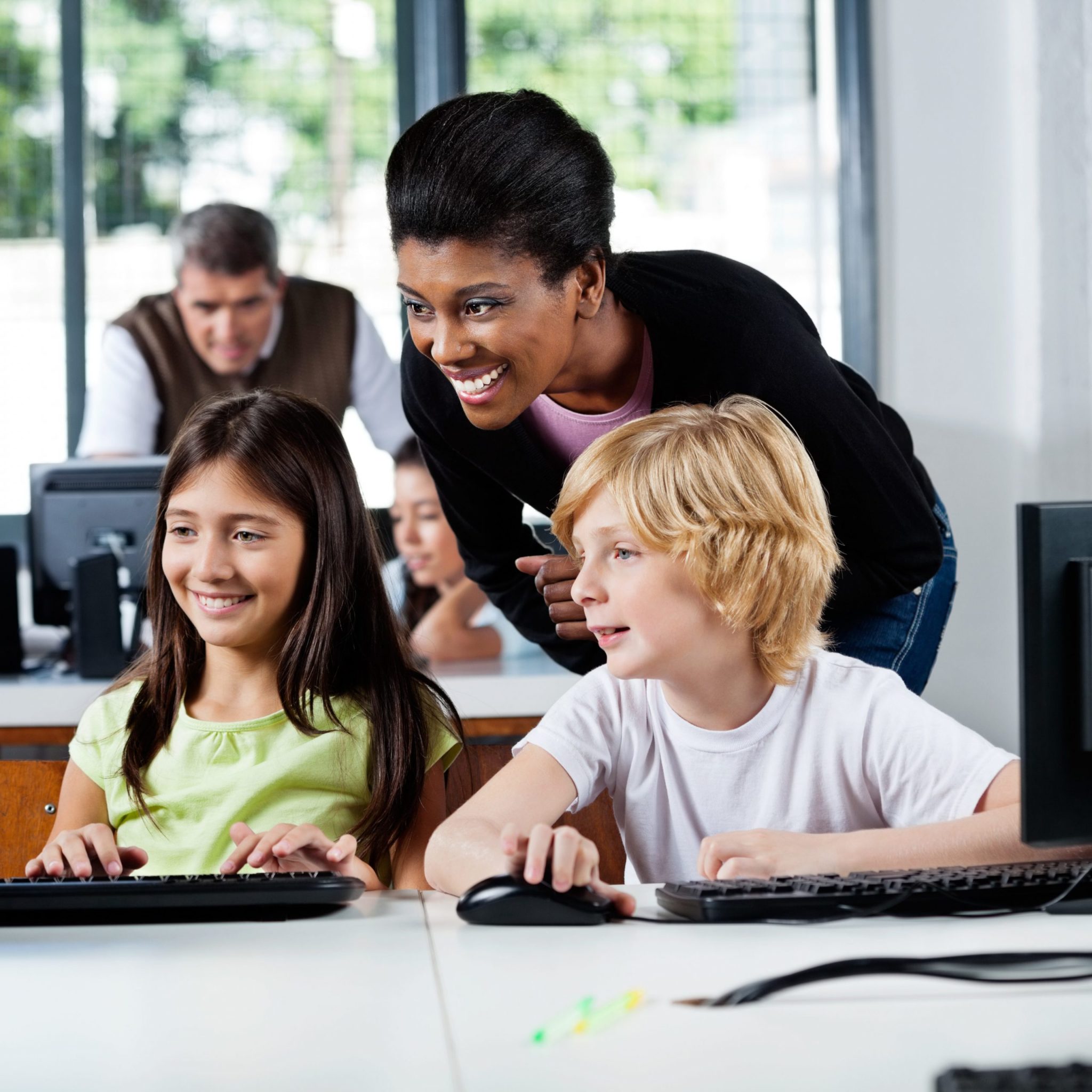 Happy female teacher assisting schoolchildren in using computer at school