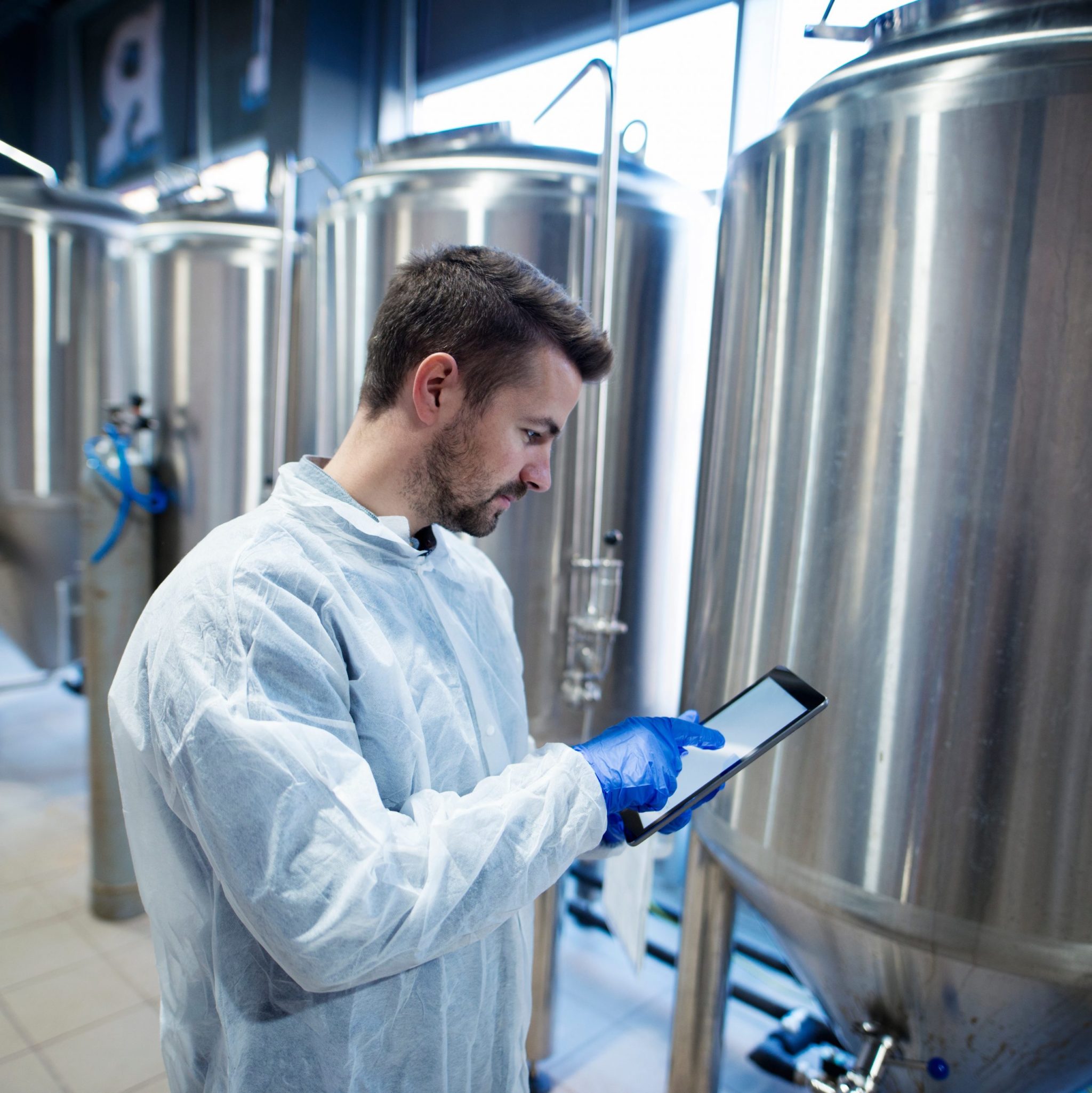 A man wearing plastic gloves and productive gear working on a tablet in an agricultural setting. 