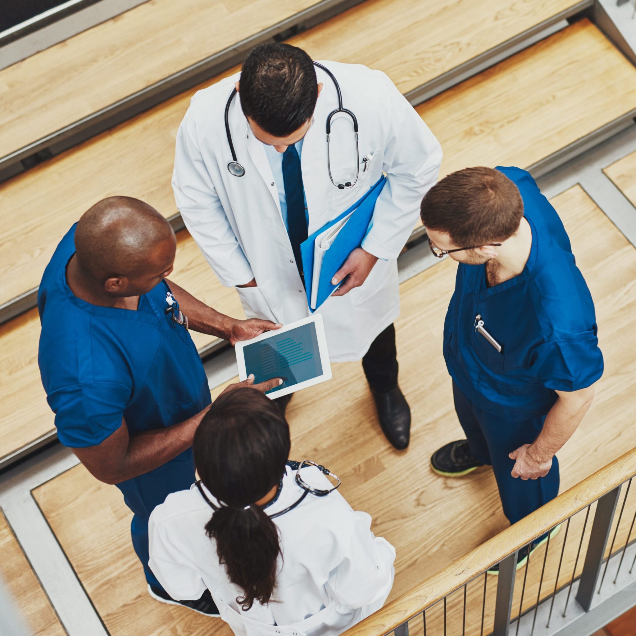 Four medical professionals standing together all looking at a tablet to help them do their jobs.