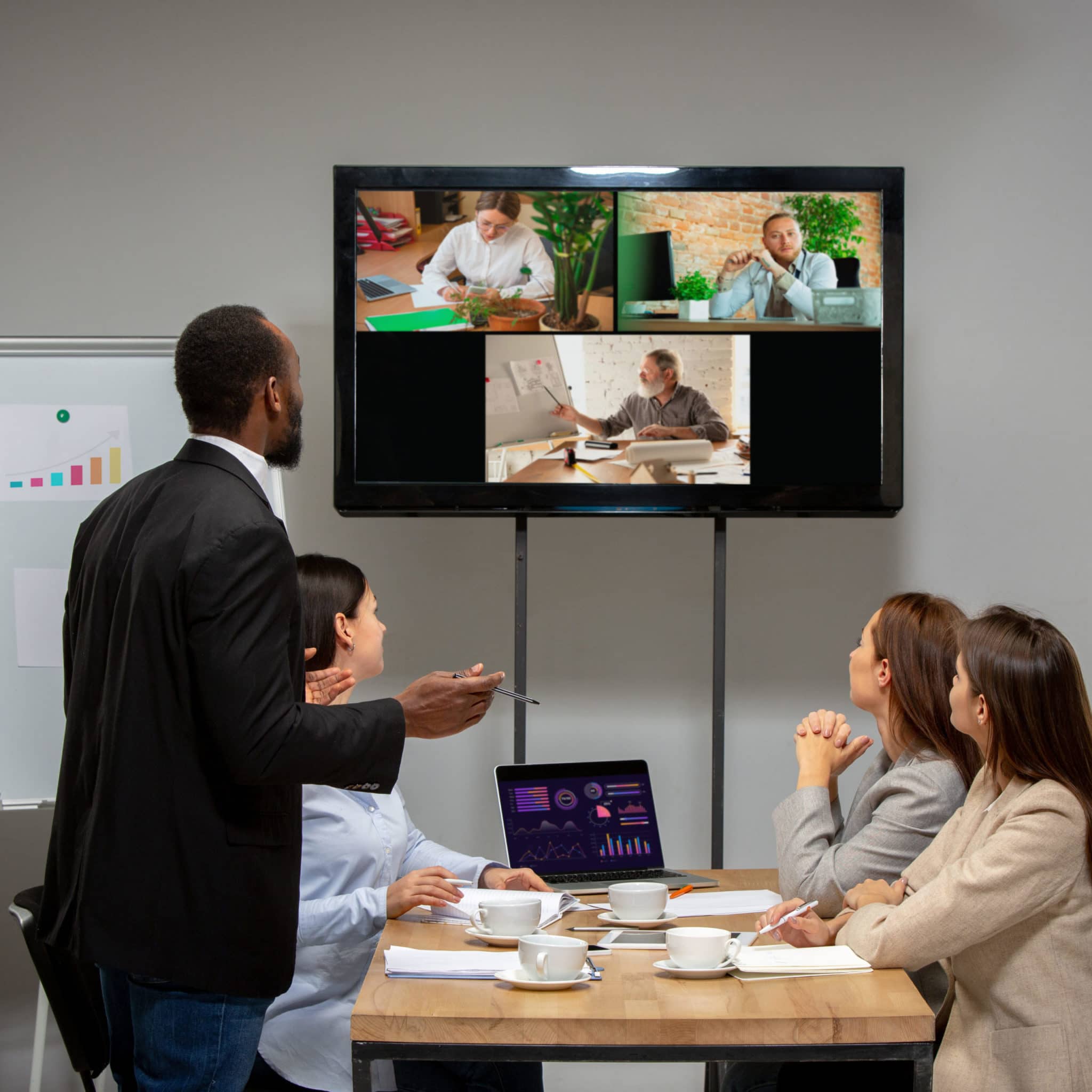 Four associates meeting in a board room while on a zoom call with three additional people.