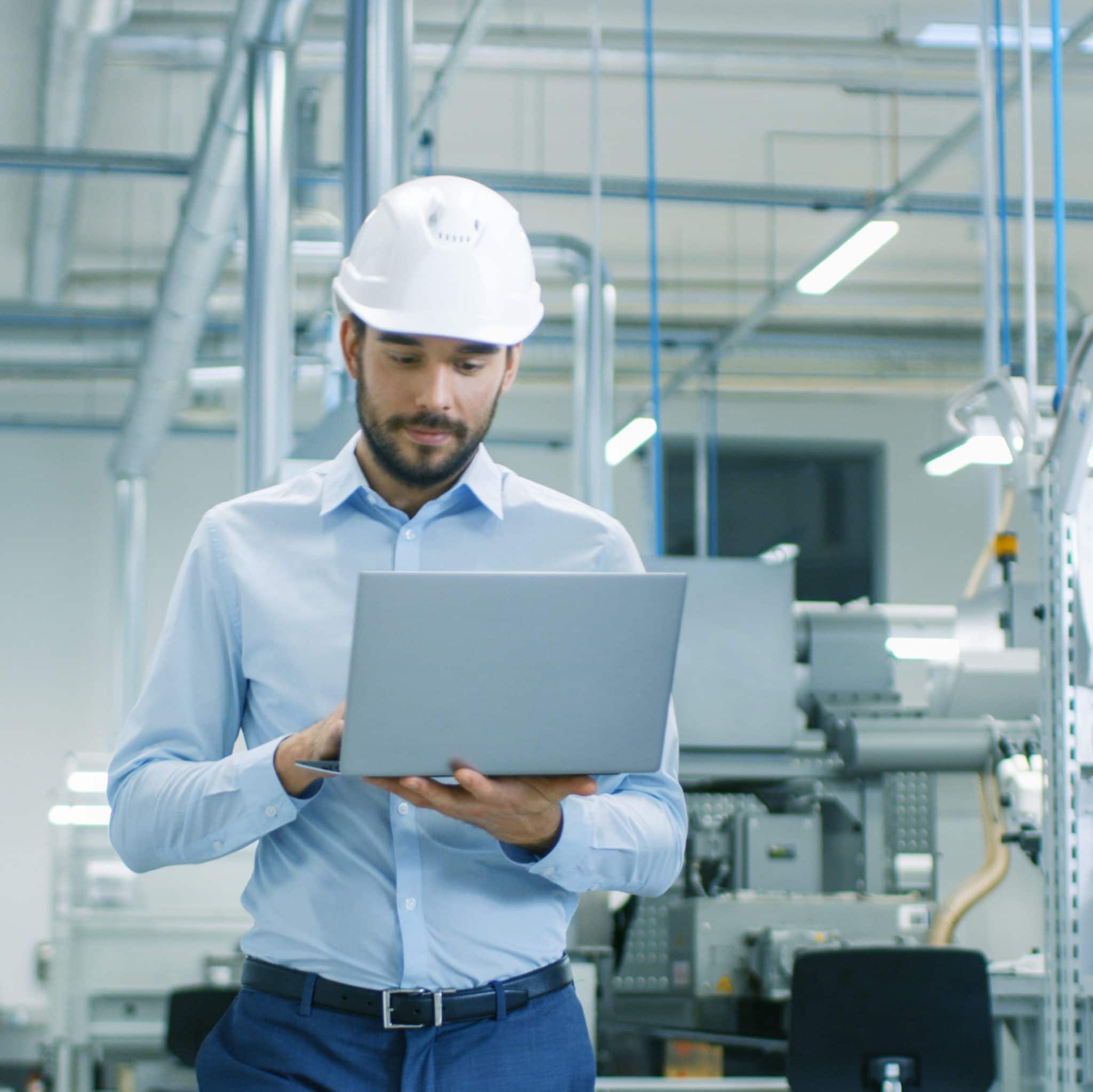 Male engineer wearing hard hat walking with laptop computer.