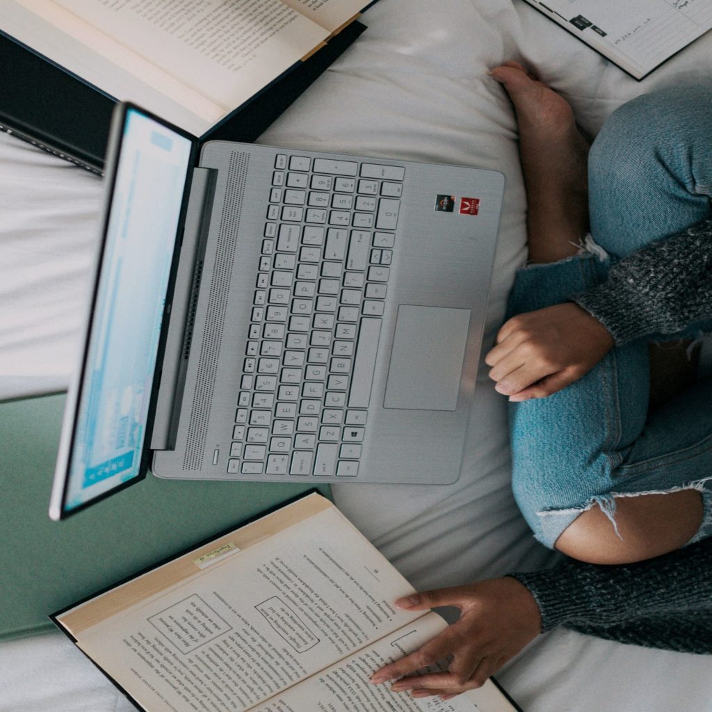 College students sitting on their bed with various books open as well as their laptop computer.