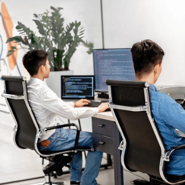 Two SysAdmins sitting at their work desks looking at computer monitors running Privilege Manager.