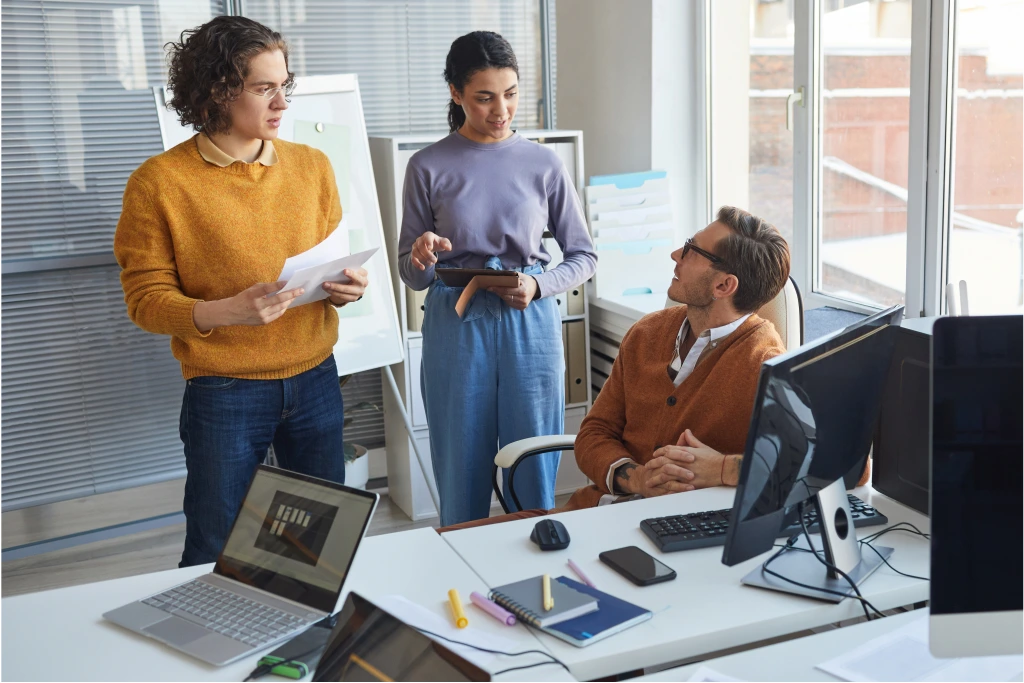 Office workers around a desk discussing the benefits of Recast Software products and their endpoint management software solutions.