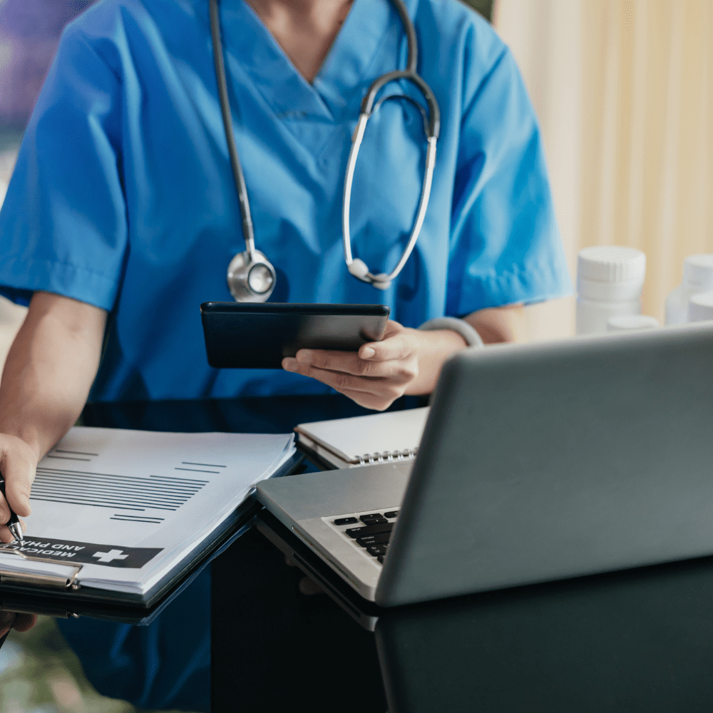 A medical professional using a laptop while filling out paperwork.