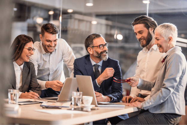 Team of business professionals gathering around computers all laughing.